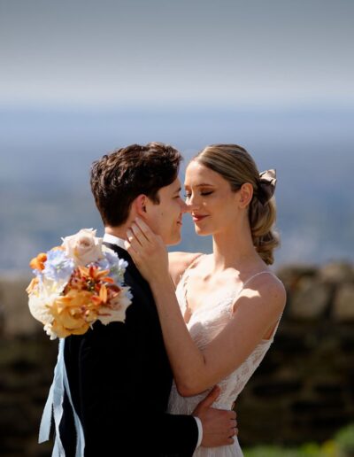 Hochzeitspaar umarmt sich eng, die Braut hält einen Blumenstrauß mit orangefarbenen Blüten