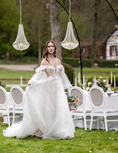 Braut im weißen Kleid steht draußen vor weißen Stühlen, Dekoration mit Blumen und Kronleuchtern
